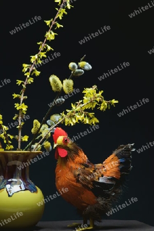 Ein Huhn als Dekoration. In der Mitte eine gelbe Vase mit einem Strauss Weide und Forsythie.