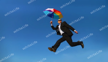 Man in suit with coloured umbrella under a blue sky - Mann in Anzug mit buntem Regenschirm unter blauem Himmel                               