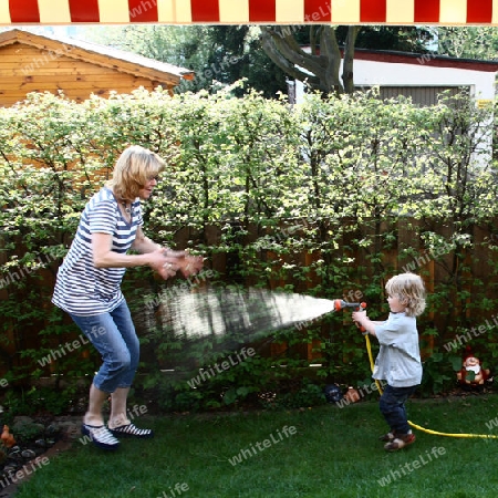 Kind spritzt Frau mit Wasser nass