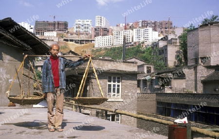 a men in the old city with the new city in the back in the city of wushan on the yangzee river near the three gorges valley up of the three gorges dam project in the province of hubei in china.