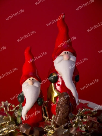 Zwei rote Weihnachtsmaenner, ein Schokoladenweihnachtsmann vor rotem Hintergrund.