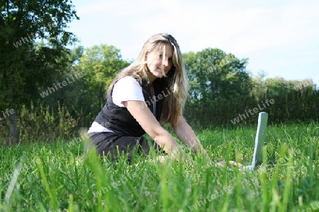 Frau auf Wiese mit Laptop l?chelt