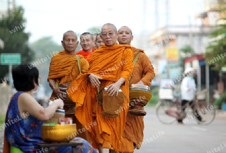 Moenche auf ihrem Rundgang am fruehem Morgen vor dem Tempel in der Stadt Tha Khaek in zentral Laos an der Grenze zu Thailand in Suedostasien.