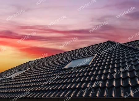 Open roof window in velux style with black roof tiles during sunset