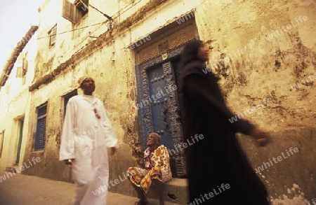  Ein Mann aus Zanzibar in traditionelle Kleidung steht an einer alten Holztuer inmitten der Altstadt Stone Town der Hauptstadt Zanzibar Town auf der Insel Zanzibar welche zu Tansania gehoert.     