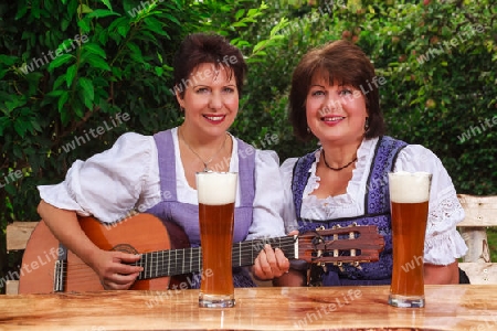 ?ltere bayerische Frauen sitzen im Dirndl zusammen und musizieren bei einer gem?tlichen halbe Wei?bier