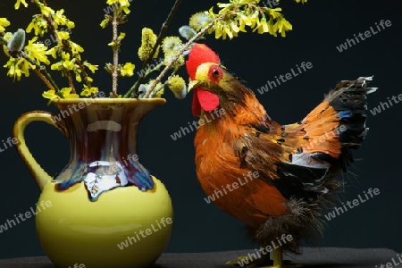 Ein Huhn als Dekoration. In der Mitte eine gelbe Vase mit einem Strauss Weide und Forsythie