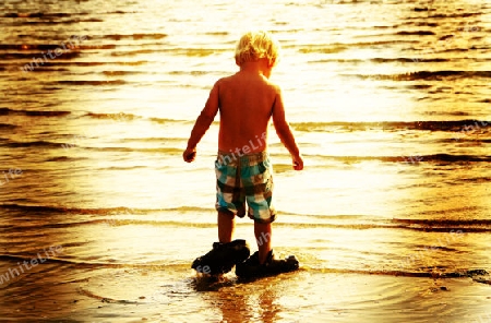 Young boy with daddys shoes on the beach at sunset