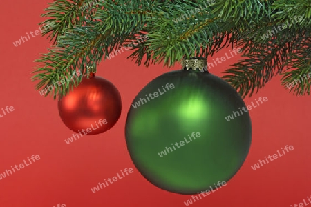 Dekorative Weihnachtskugel an einem Tannenzweig auf rotem Hintergrund