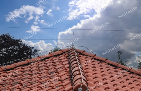 A roof with red shingles and a lightning conductor on it