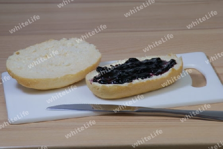 Halbiertes Br?tchen mit einer rohen und einer, mit Heidelbeermarmelade, geschmierten H?lfte.