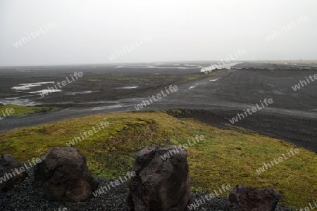 Der S?den Islands, Parkplatz vor trostloser Asche-Landschaft mit Steinen im Vordergrund, am  malerischen Wasserfall Skogafoss, der hier in einer Breite von 25 Metern bis zu 60 Meter tief ?ber die Flu?kante des Sk?g? herabst?rzt