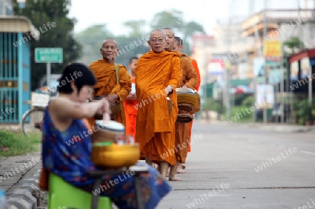 Moenche auf ihrem Rundgang am fruehem Morgen vor dem Tempel in der Stadt Tha Khaek in zentral Laos an der Grenze zu Thailand in Suedostasien.