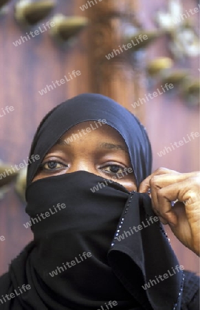 Eine Frau aus Zanzibar in traditionelle Kleidung im Portrait inmitten der Altstadt Stone Town der Hauptstadt Zanzibar Town auf der Insel Zanzibar welche zu Tansania gehoert.         